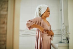 Young Asian woman standing in front of bathroom mirror while doing breast self-examination