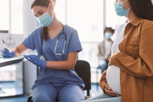 Pregnant Lady In Mask On Appointment At Doctor's Office